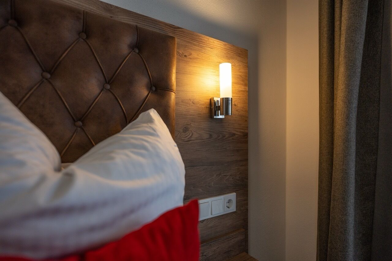 Un dormitorio con cabecera capitonada, una lámpara de pared y un enchufe.