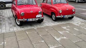 Two vintage red cars parked on a paved sidewalk.