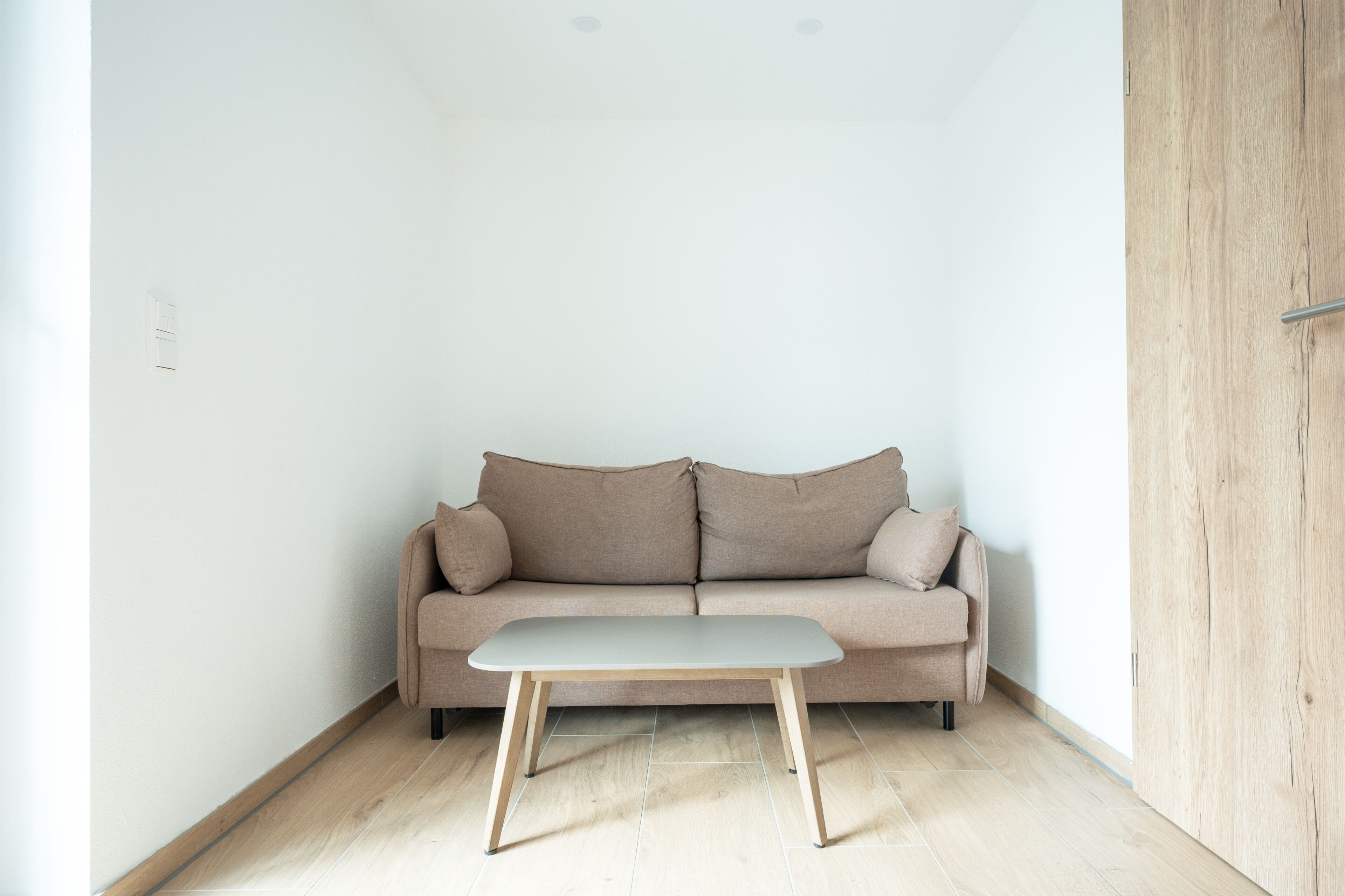 A minimalist room with a beige sofa, a small table, and a wooden door.