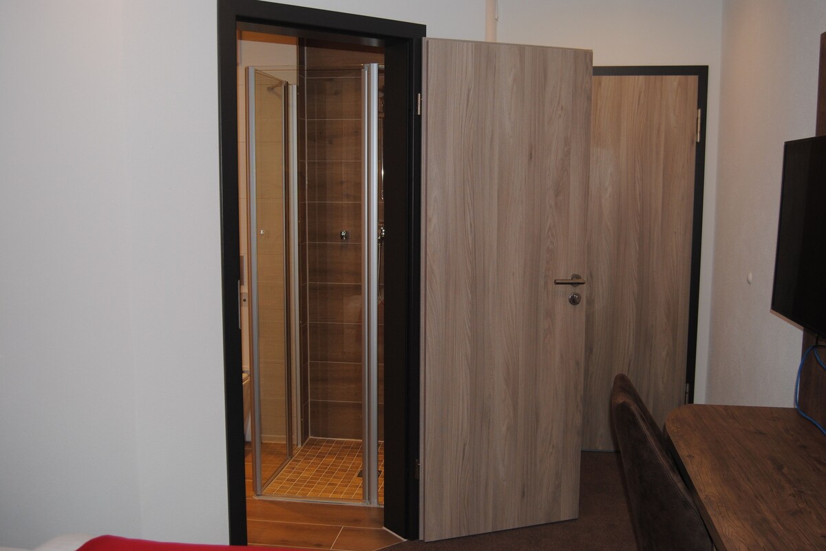 Une pièce avec une porte en bois, un banc et un espace douche.
