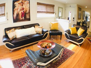A living room with a black leather sofa, a glass coffee table, and a patterned rug.