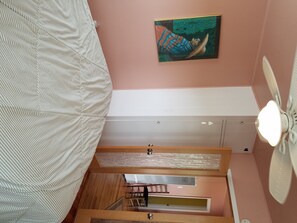 Une chambre à coucher avec un lit, un ventilateur de plafond, un tableau et une fenêtre.