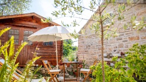 Une cabane en bois avec un mur en pierre, un espace extérieur aménagé avec une table et des chaises, et des plantes en pot.