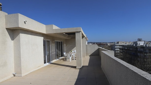 Terraza en la azotea con vistas a la ciudad, zona de estar techada y una pequeña mesa.