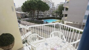 Ein Balkon mit Tisch und Stühlen, einem kleinen Blumentopf und Blick auf einen Swimmingpool sowie Gebäude im Hintergrund.