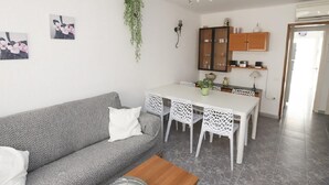 Ein modernes Wohnzimmer mit grauem Sofa, weißen Stühlen, einem Holztisch und einem Esstisch mit weißer Spitzenwäsche.