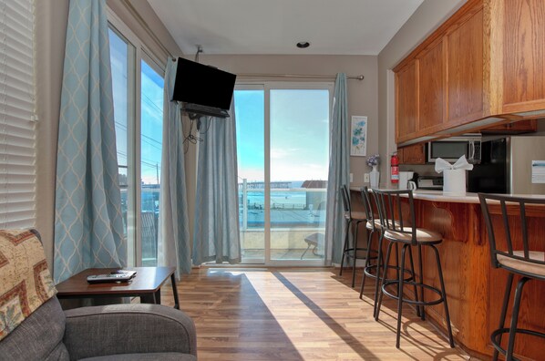 A modern kitchen with a bar area, a flat-screen TV, and a view through the glass doors.