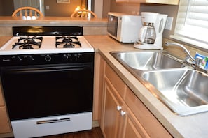 Una cocina equipada con estufa, microondas, cafetera y un lavamanos doble.