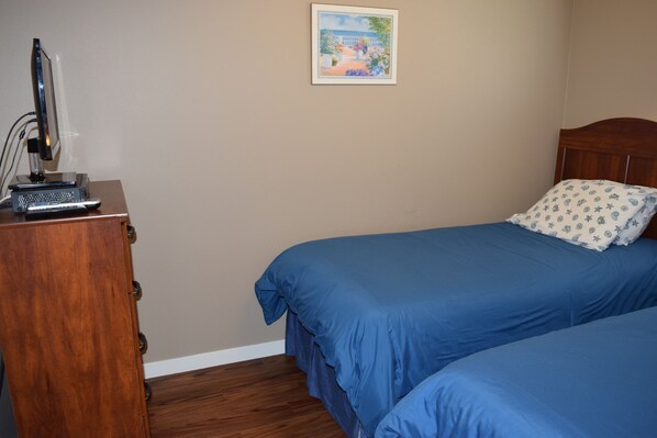 A bedroom with two single beds, a wooden desk with a computer, and a framed picture on the wall.