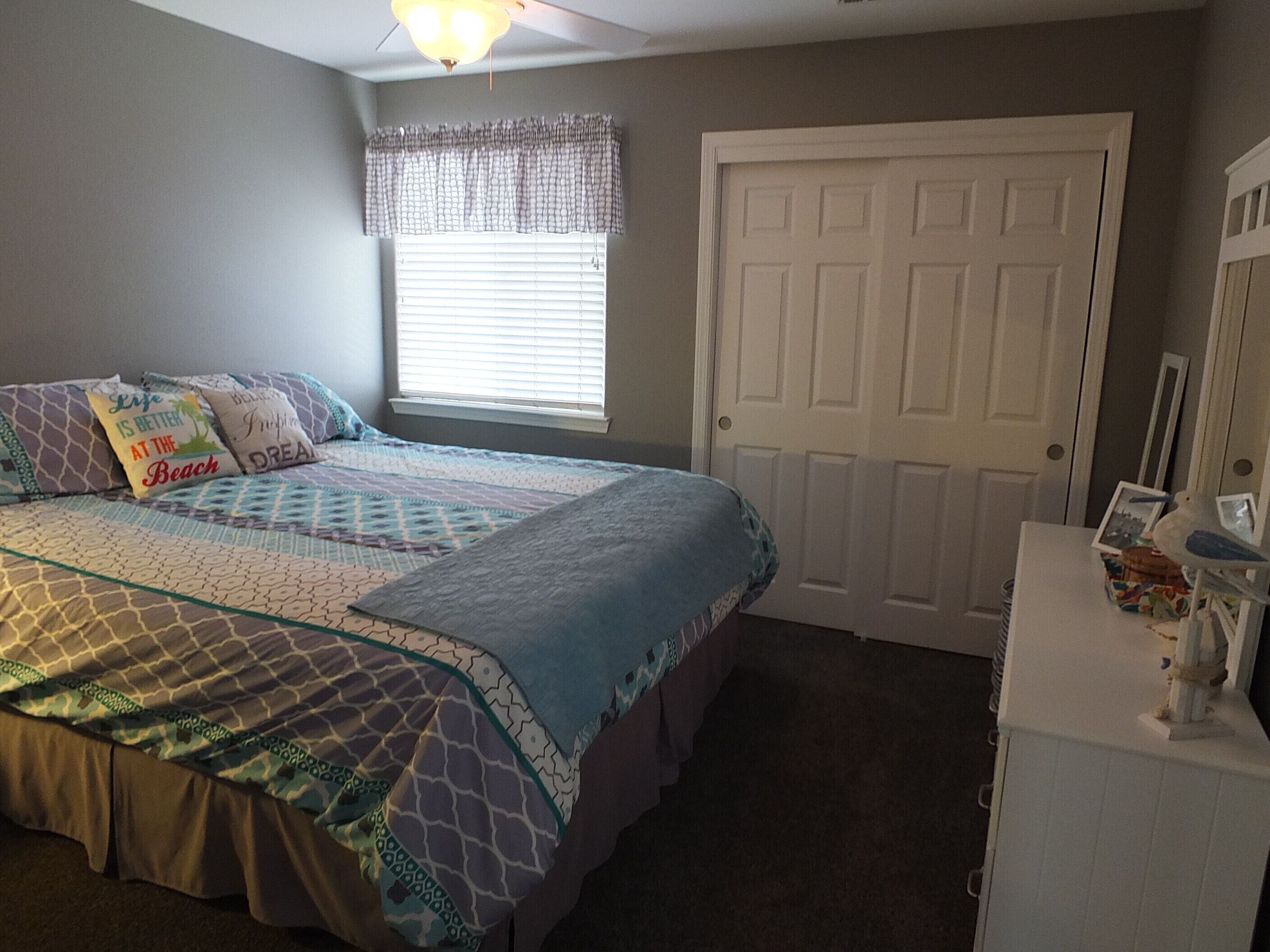 A bedroom with a bed, a window with blinds, a door, and a dresser with a bird decoration.