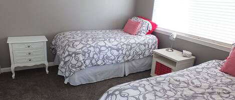 Quarto com duas camas, uma mesinha de cabeceira e uma escrivaninha com abajur.