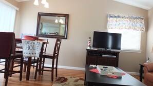 A dining area with a table and chairs, a television, and a kitchen in the background. - 618 Airpark: 2  BR, 2  BA Condominium in Oceano, Sleeps 4 (Oceano)