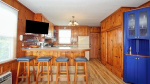 A kitchen with wooden cabinets, a central island with stools, a built-in TV, and a blue cabinet with glass doors. - 141 A 1st Street: 3  BR, 2  BA House in Avila Beach, Sleeps 6 (Avila Beach)