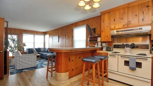 A kitchen with wooden cabinets, a bar area with stools, a stove, and a dining area with a sofa and table. - 141 A 1st Street: 3  BR, 2  BA House in Avila Beach, Sleeps 6 (Avila Beach)