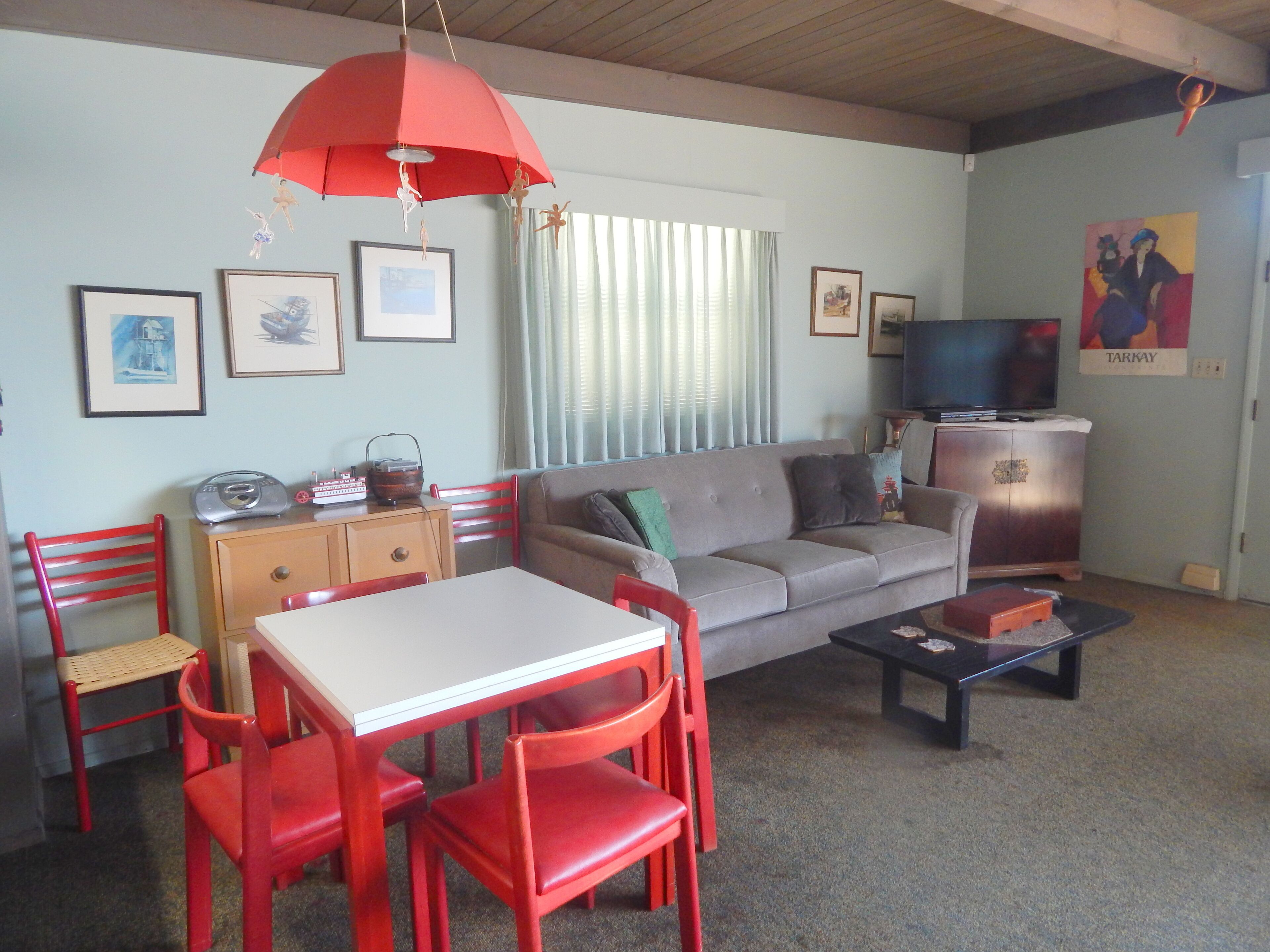 Een woonkamer met een bank, rode stoelen, een tafel, een televisie en kunstwerken aan de muur.