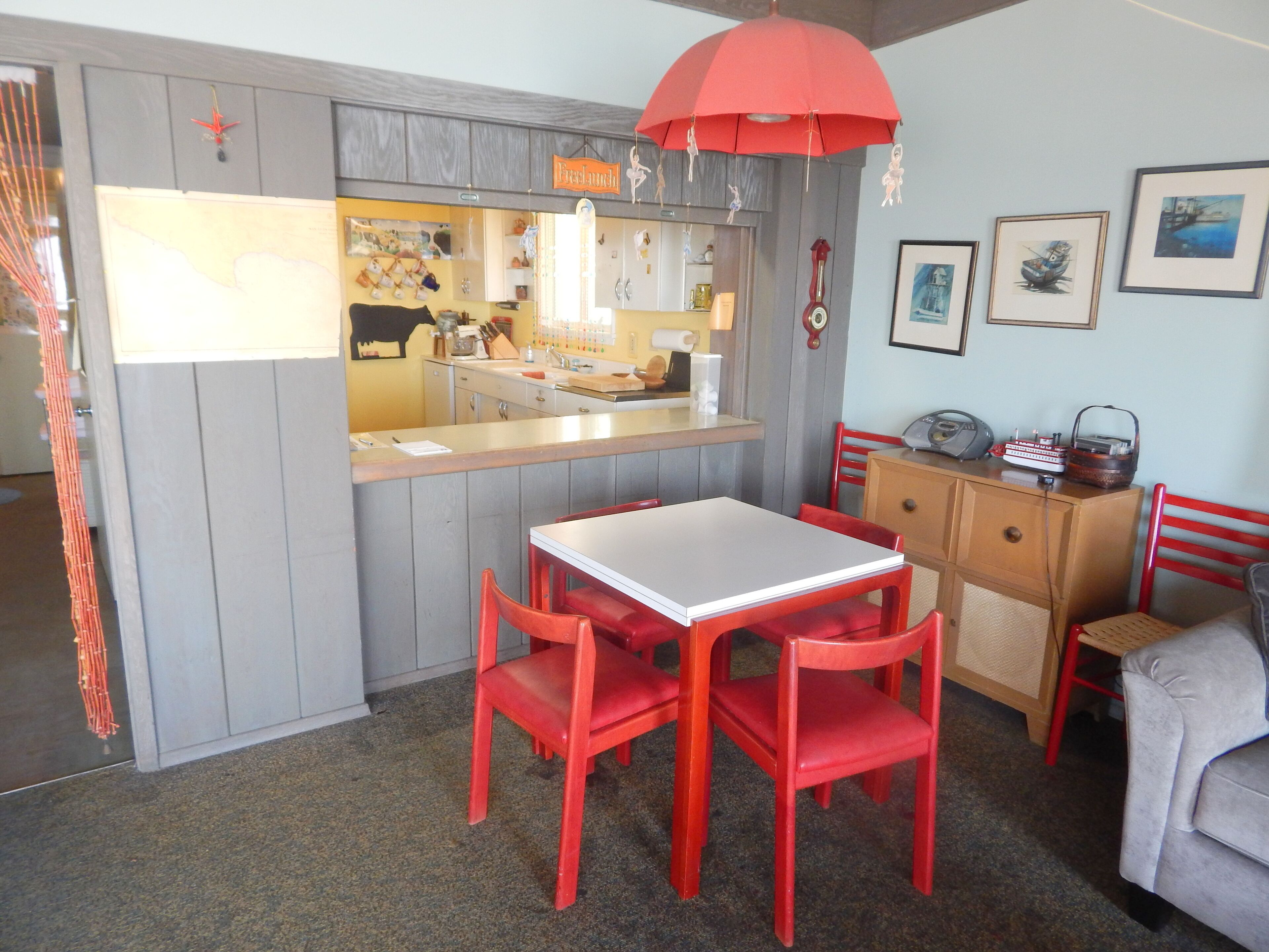 Une cuisine de taille modeste avec un îlot central, des chaises rouges et un parasol rouge suspendu au-dessus.