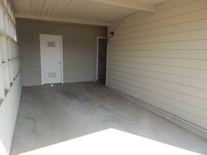 A covered outdoor area with a concrete floor, a white door, and a white exterior wall.