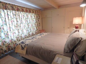 A bedroom with a large bed, floral curtains, a bedside lamp, and a wardrobe.