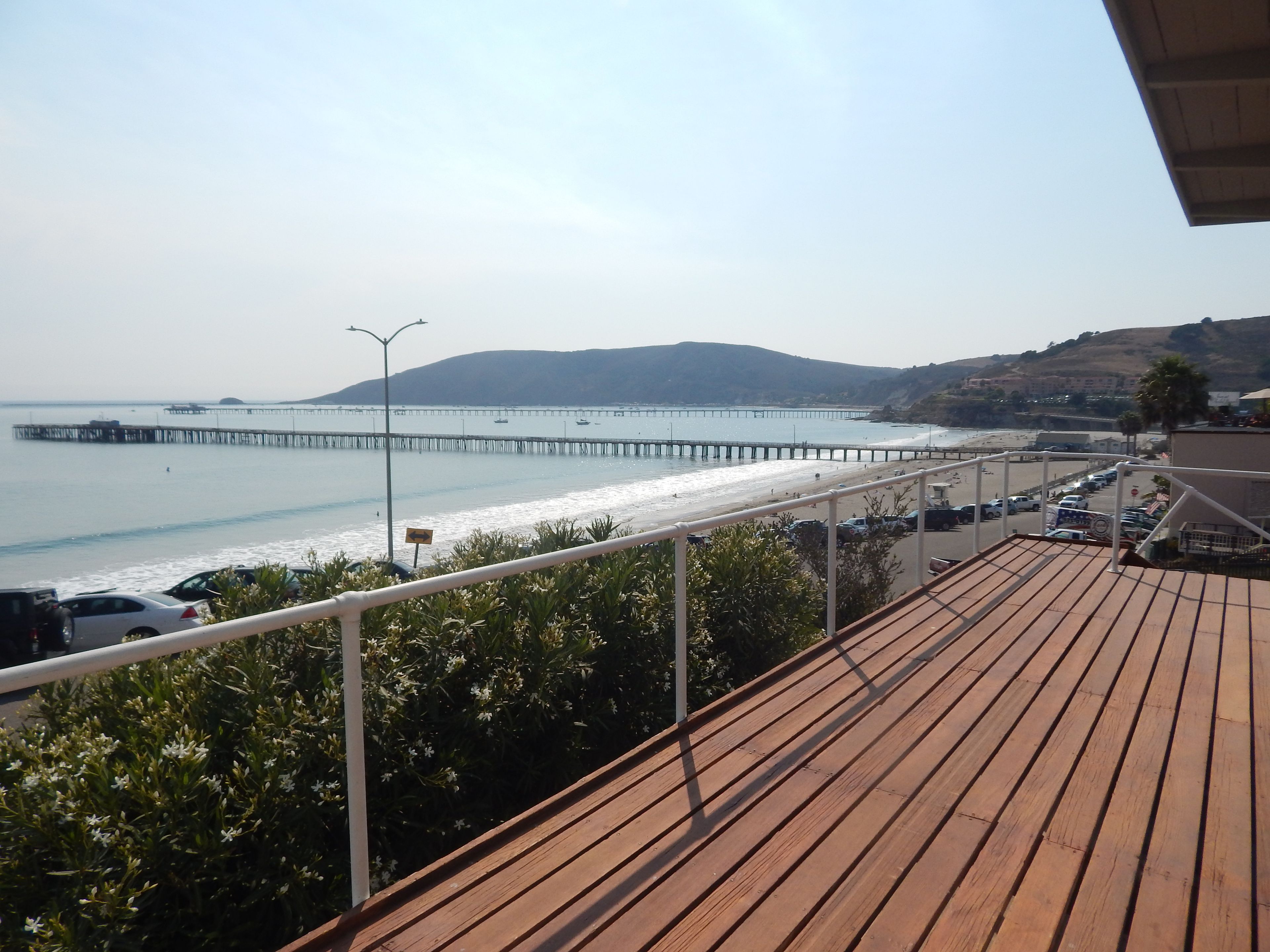 A wooden deck with a view of a beach, a pier, and distant hills.
