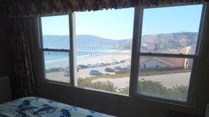 Une chambre d’hôtel avec un lit, une fenêtre donnant sur une plage, un parking et un pont visible au loin.