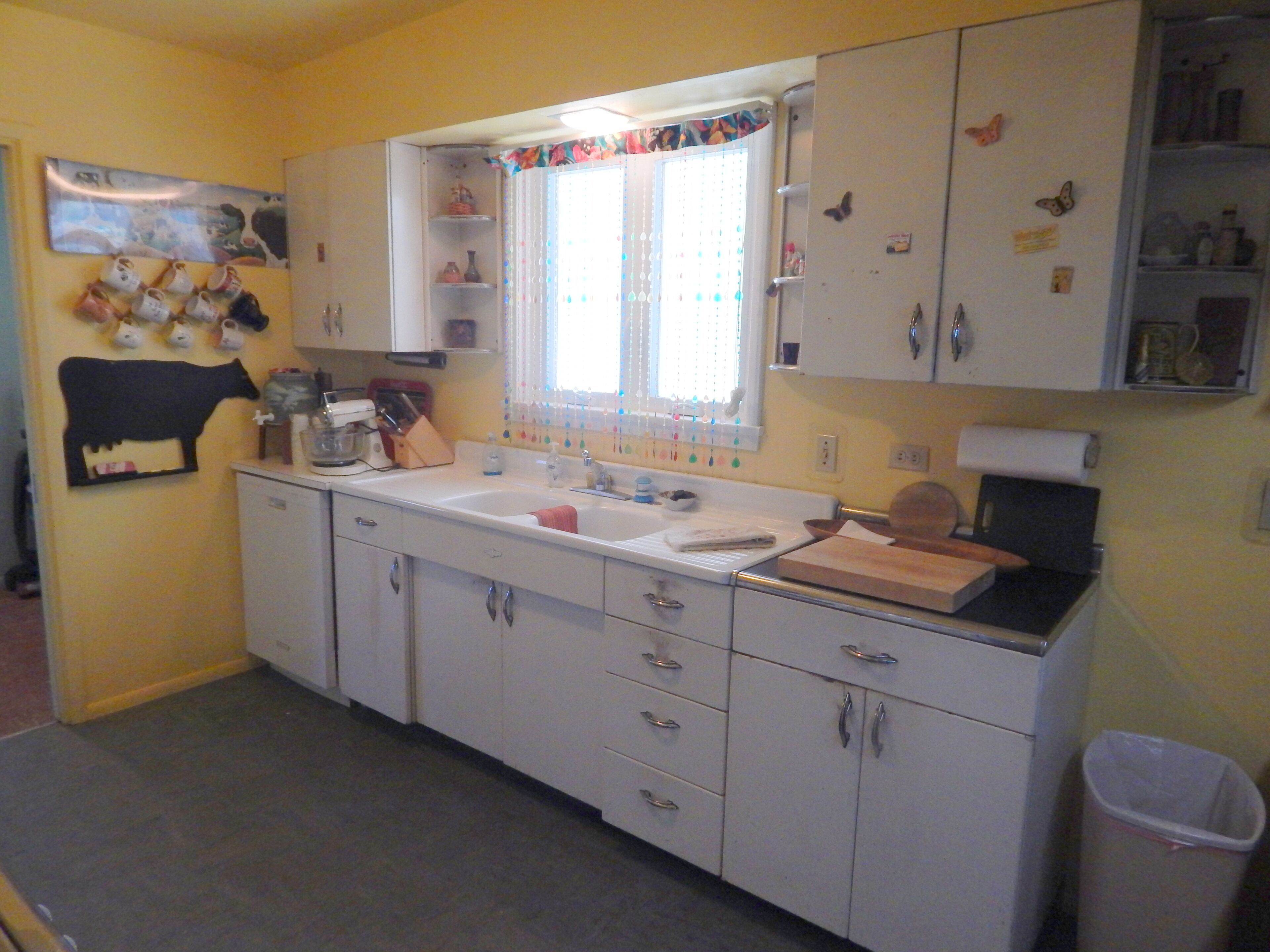 A kitchen with white cabinets, a sink, and a window with a curtain.