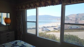 Une chambre à coucher avec un lit, une lampe et une fenêtre donnant sur une plage et une jetée.