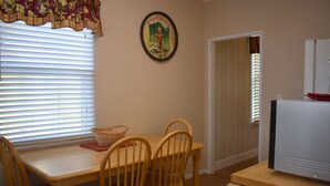 A dining area with a wooden table, four chairs, a basket, and a wall-mounted picture.