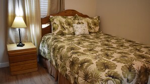 A neatly made bed with a floral bedspread, a bedside lamp, and a wooden nightstand with drawers.