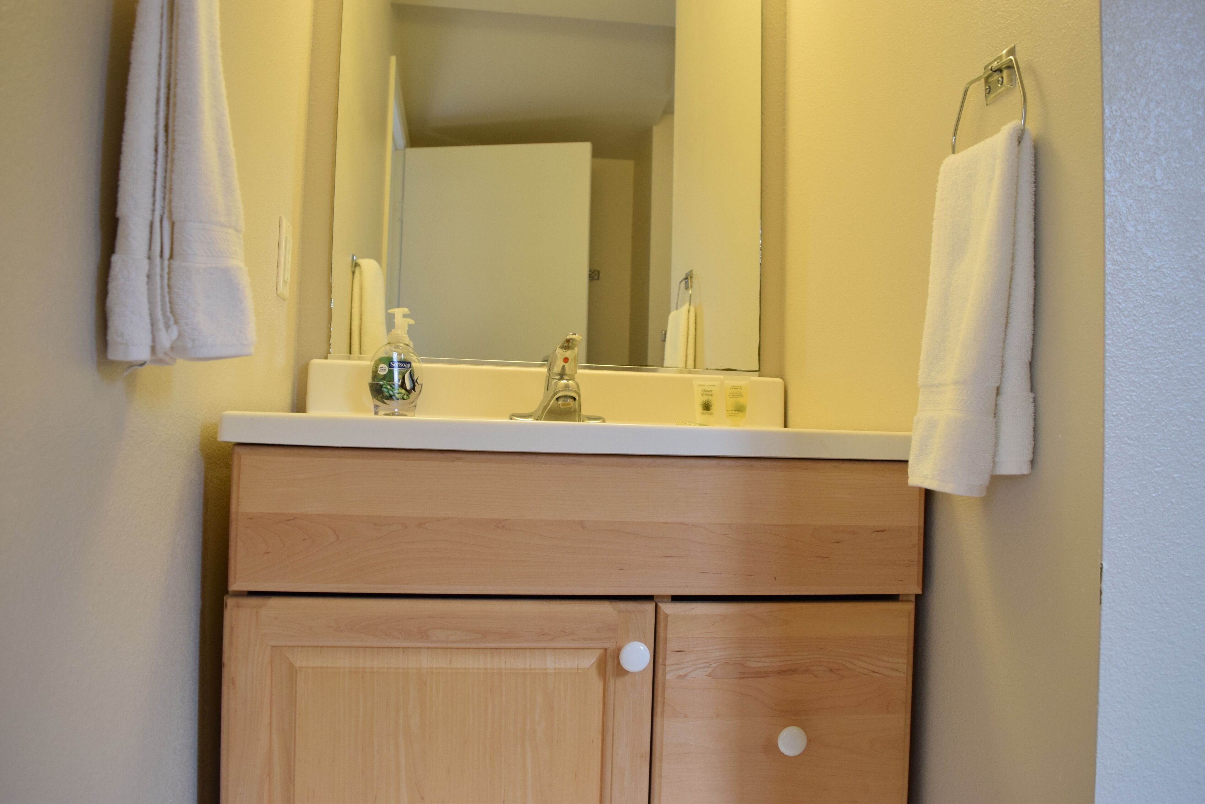 Une salle de bain avec des meubles en bois, un comptoir blanc, un miroir et deux serviettes suspendues à des crochets.