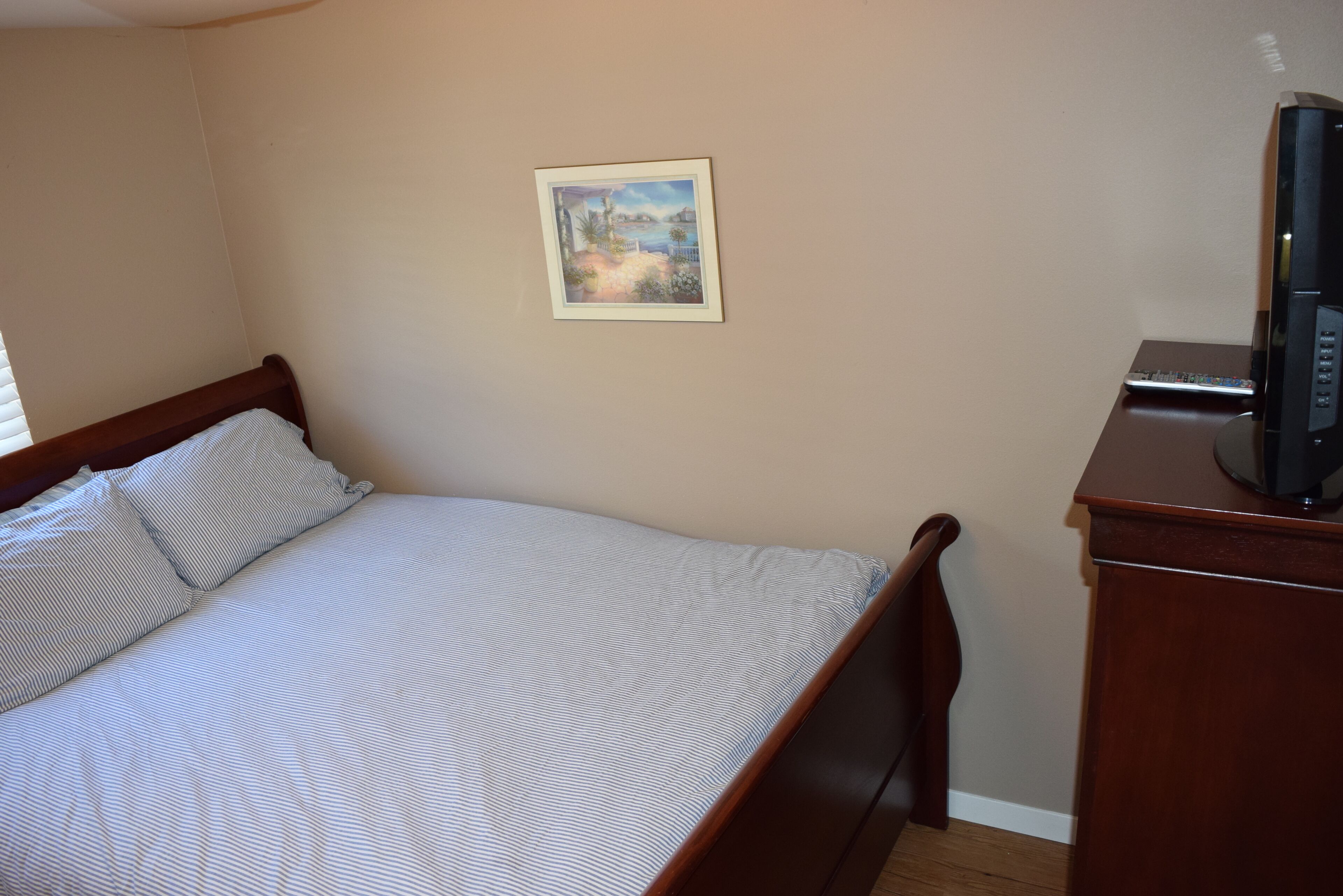 A bedroom with a bed, a painting on the wall, and a TV on a wooden stand.