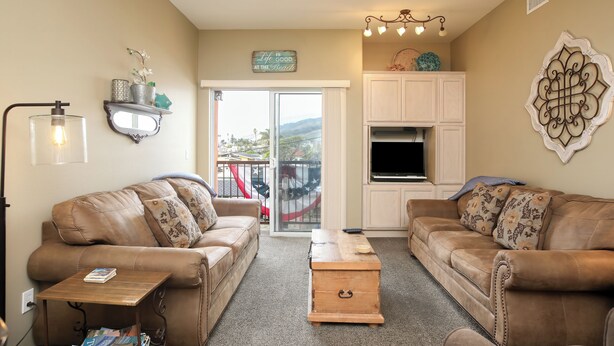 A living room with two brown leather sofas, a wooden coffee table, a TV, and a decorative wall piece. - 210 Casa Bella: 2  BR, 2  BA Condominium in Pismo Beach, Sleeps 6 (Pismo Beach)