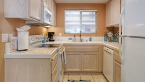 A kitchen with wooden cabinets, a white refrigerator, a dishwasher, and a window with blinds. - 210 Casa Bella: 2  BR, 2  BA Condominium in Pismo Beach, Sleeps 6 (Pismo Beach)