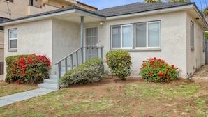 A single-story house with a covered porch, a front entrance with steps, and a small front yard with various shrubs and flowers. - 369 Stimson: 3 BR, 2 BA House in Pismo Beach, Sleeps 8 (Pismo Beach)
