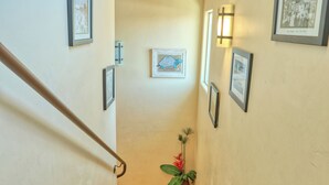 Eine Treppe mit Handlauf, gerahmte Bilder an den Wänden und ein Blumentopf am Fuß.