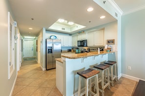 A kitchen with white cabinets, a granite countertop, a refrigerator, a microwave, and a sink.