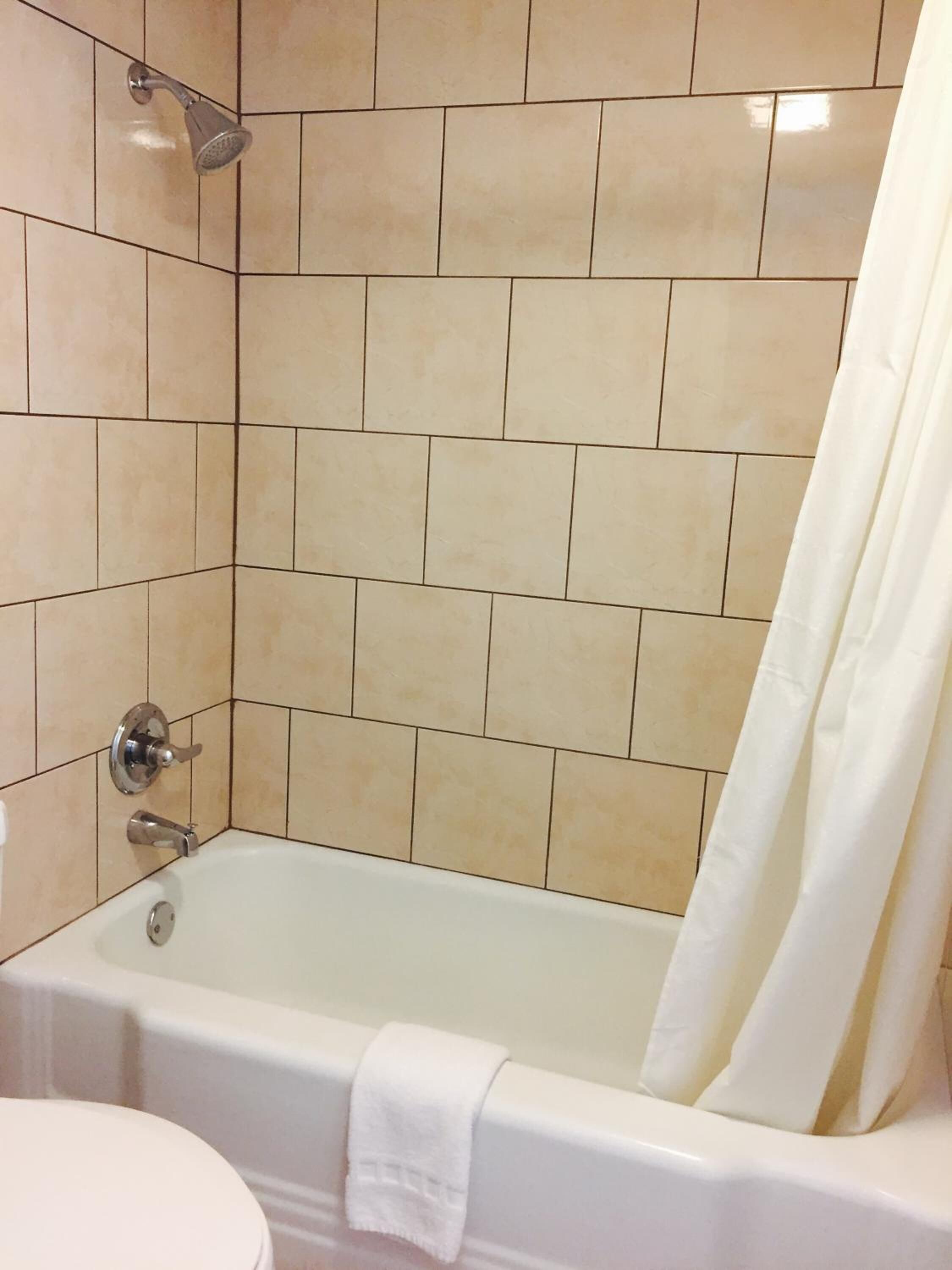 A bathroom with beige tiles, a bathtub, a showerhead, and a toilet.