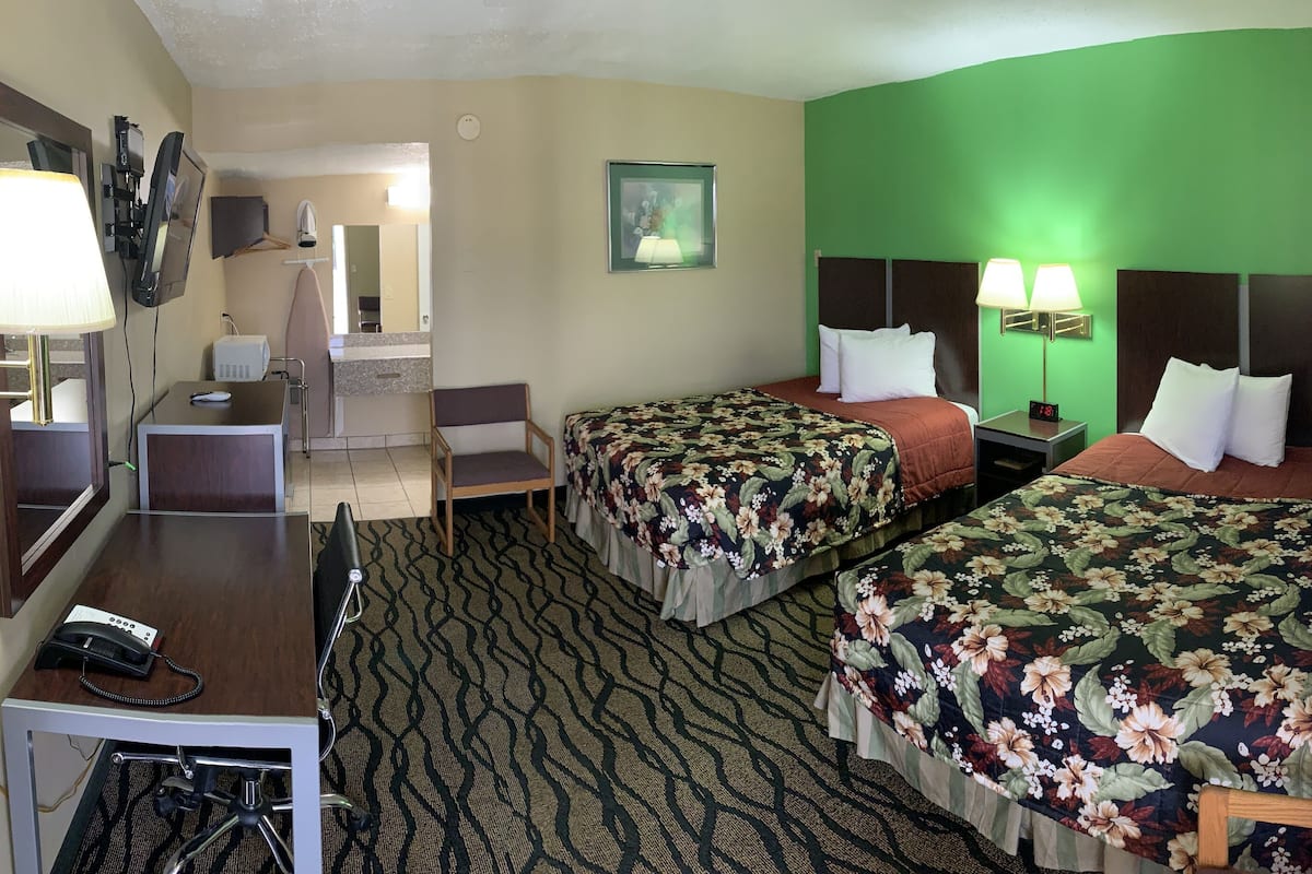 A hotel room with two beds, a desk with a telephone, a chair, a mirror, and a television.