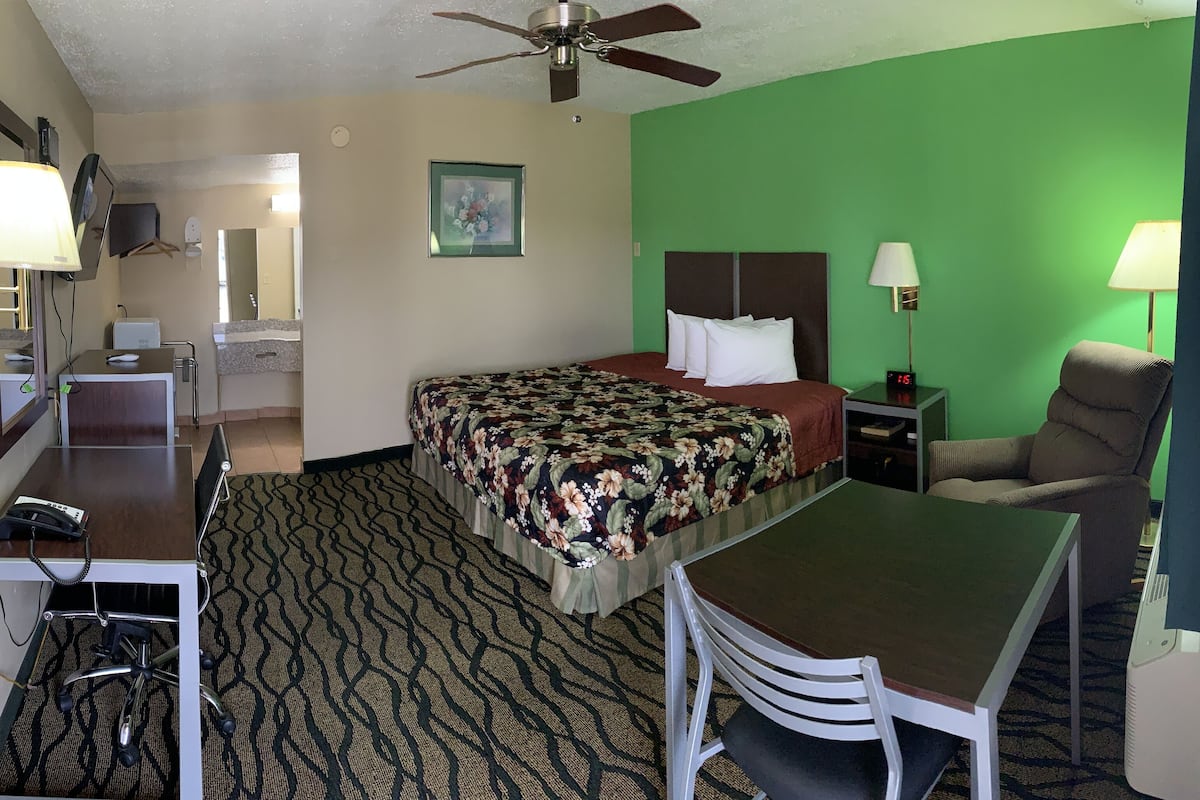 A hotel room with a bed, desk, chair, and a ceiling fan.