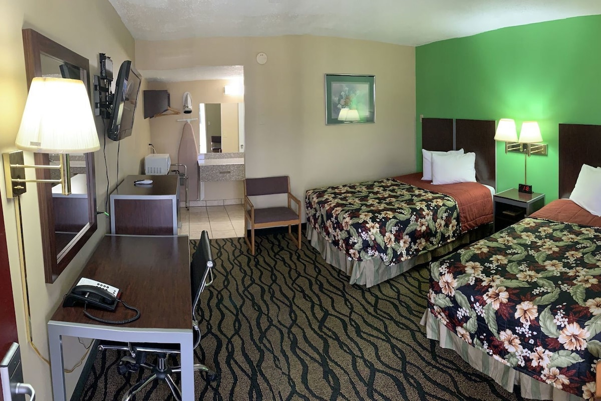 Una habitación de hotel con dos camas, un escritorio, una silla, un espejo y un televisor.