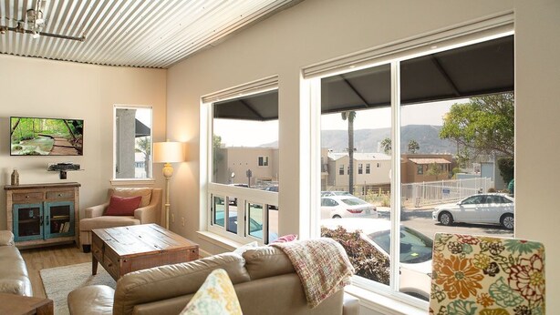 Ein Wohnzimmer mit einer Couch, einem Couchtisch, einem Fernseher und einem Fenster mit Blick auf die Straße.