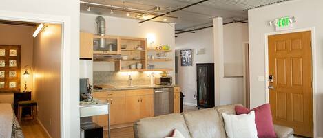 A modern living room with a sofa, a dining table, and a kitchen area with wooden cabinets and a microwave.