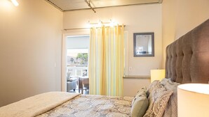 Ein Schlafzimmer mit Bett, Vorhängen, einem Spiegel und Blick auf einen Außenbereich mit Sitzgelegenheiten.