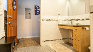 Ein Badezimmer mit Waschtisch aus Holz, weißen Fliesen, einem Handtuchhalter und einer Tür mit einem blauen Schild.