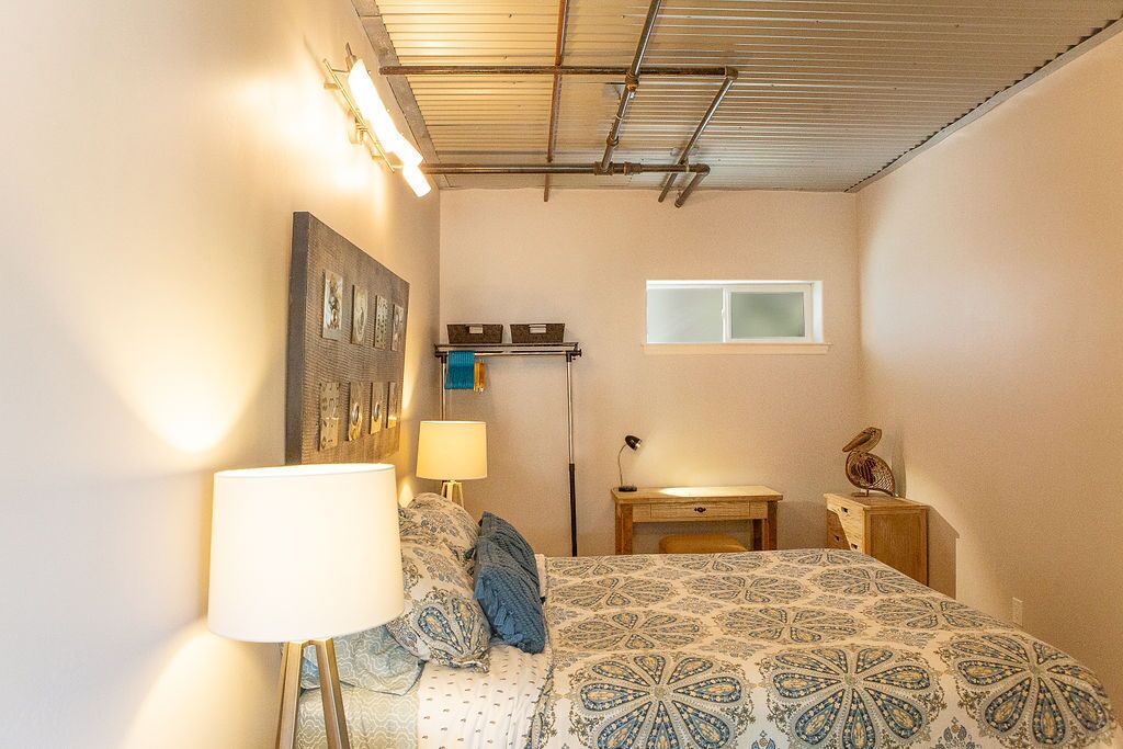 A bedroom with a bed, bedside lamps, a desk, a window, and a wall-mounted shelf.