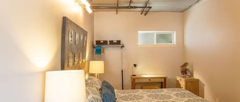 A bedroom with a bed, bedside lamps, a desk, a window, and a wall-mounted shelf.