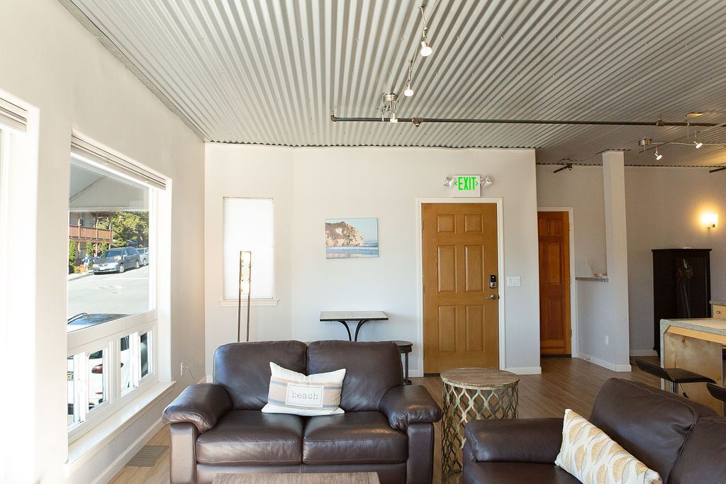 A modern living room with leather sofas, a small round table, and a view of the street through large windows.
