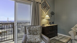 Un balcon donnant sur la ville, une chaise en osier avec un coussin à motifs, une commode en bois foncé et une lampe.