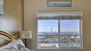 Une chambre avec une grande fenêtre, un lit avec une literie à motifs, une lampe de chevet et un tableau encadré au mur.
