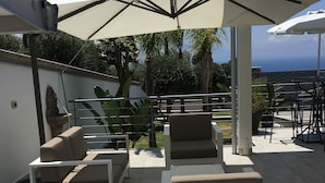 An outdoor patio area with white lounge chairs and a large umbrella, overlooking a scenic view.