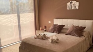 A bedroom with a large bed, a bedside table with a lamp, and a view through a sliding door.